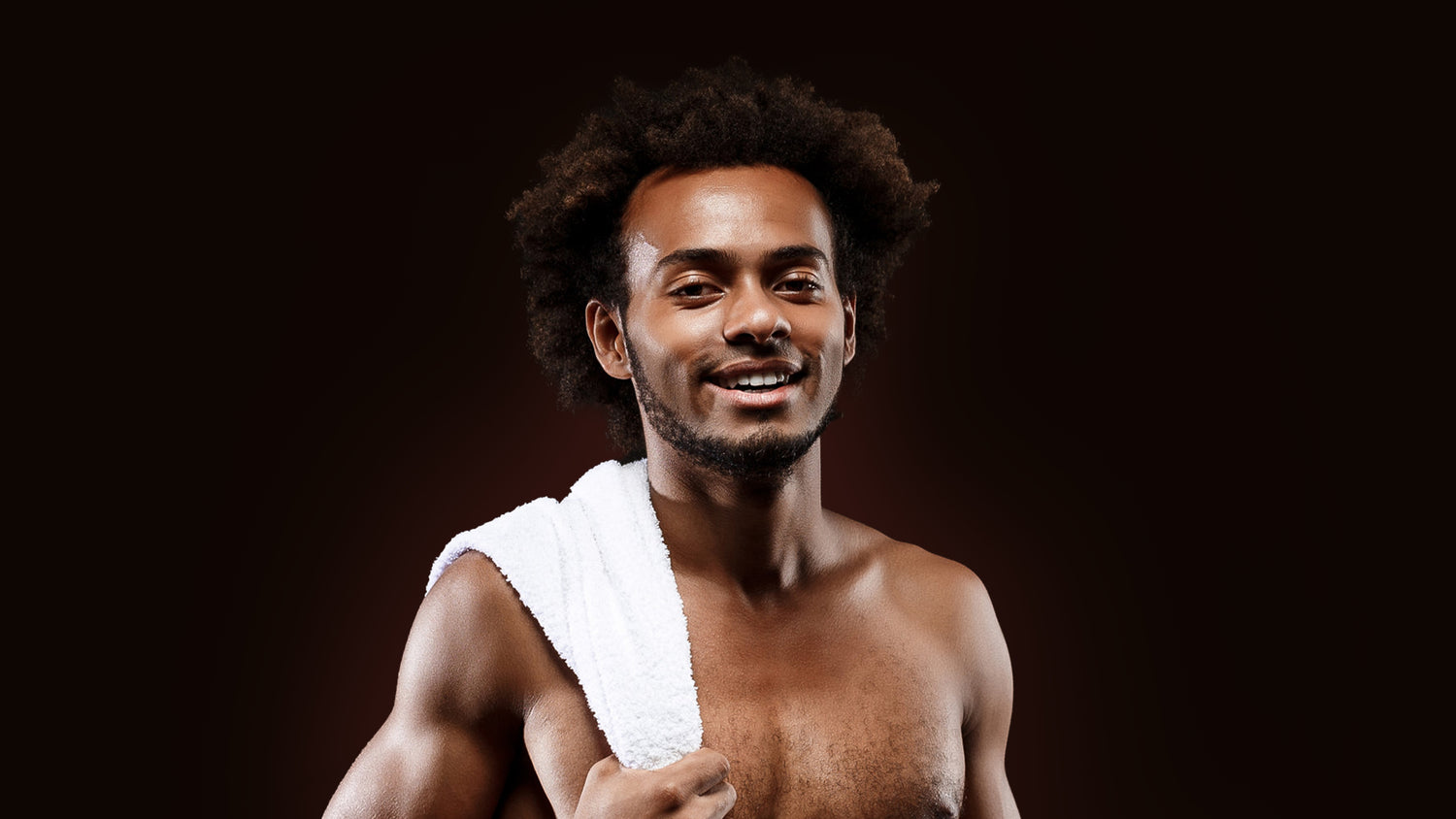 A Black Background image of a Happy Confident Man holding a white towel on his shoulder.